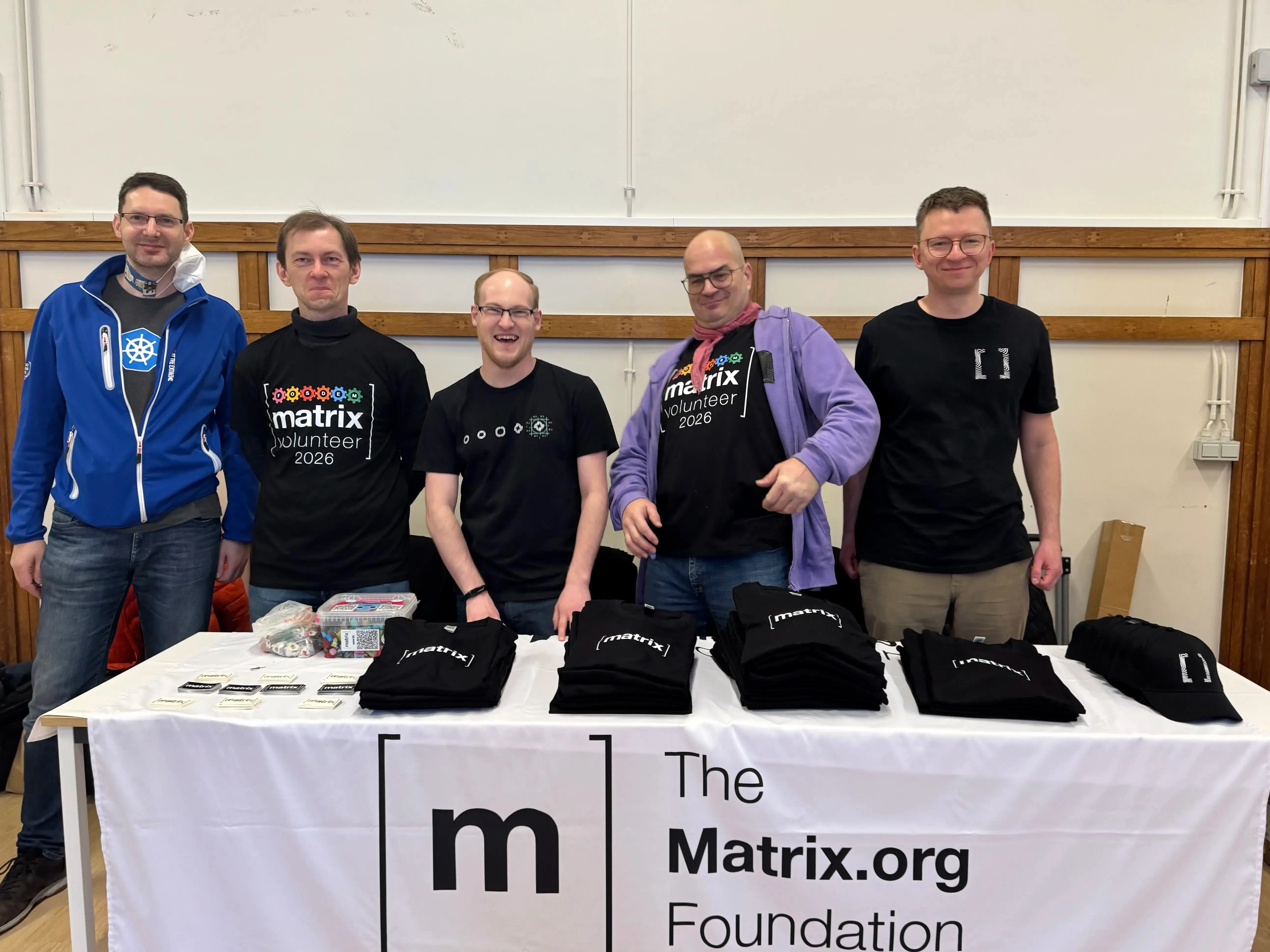 A team of people making goofy faces and laughing, behind a Matrix.org Foundation branded booth.