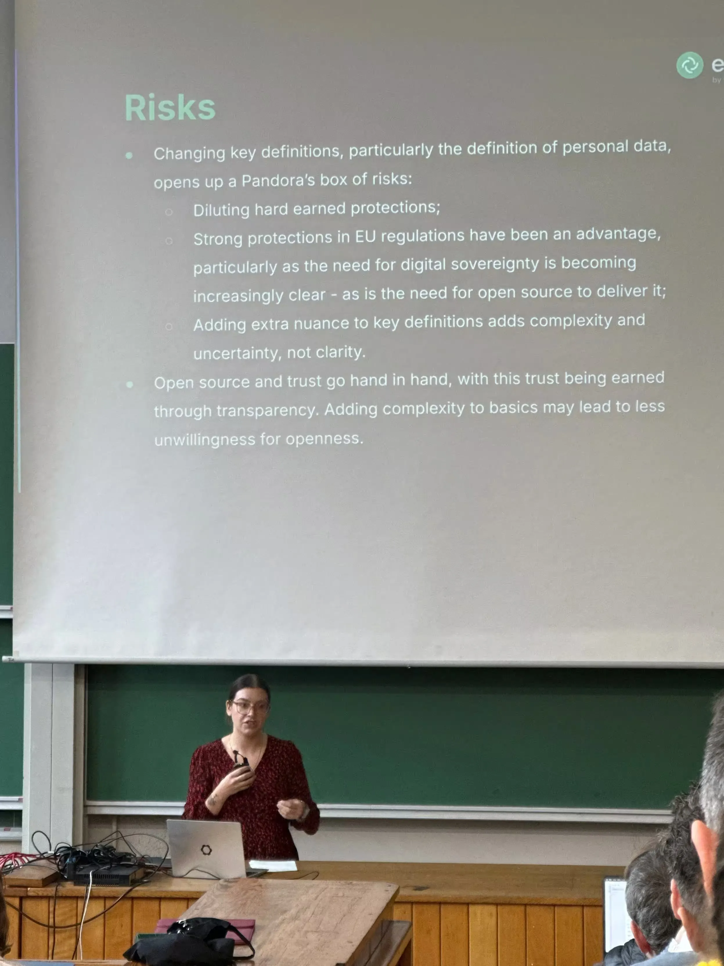 A picture of Denise, a speaker giving a talk, in front of her slides. Her slides mention risks from the upcoming Digital Omnibus regulation.