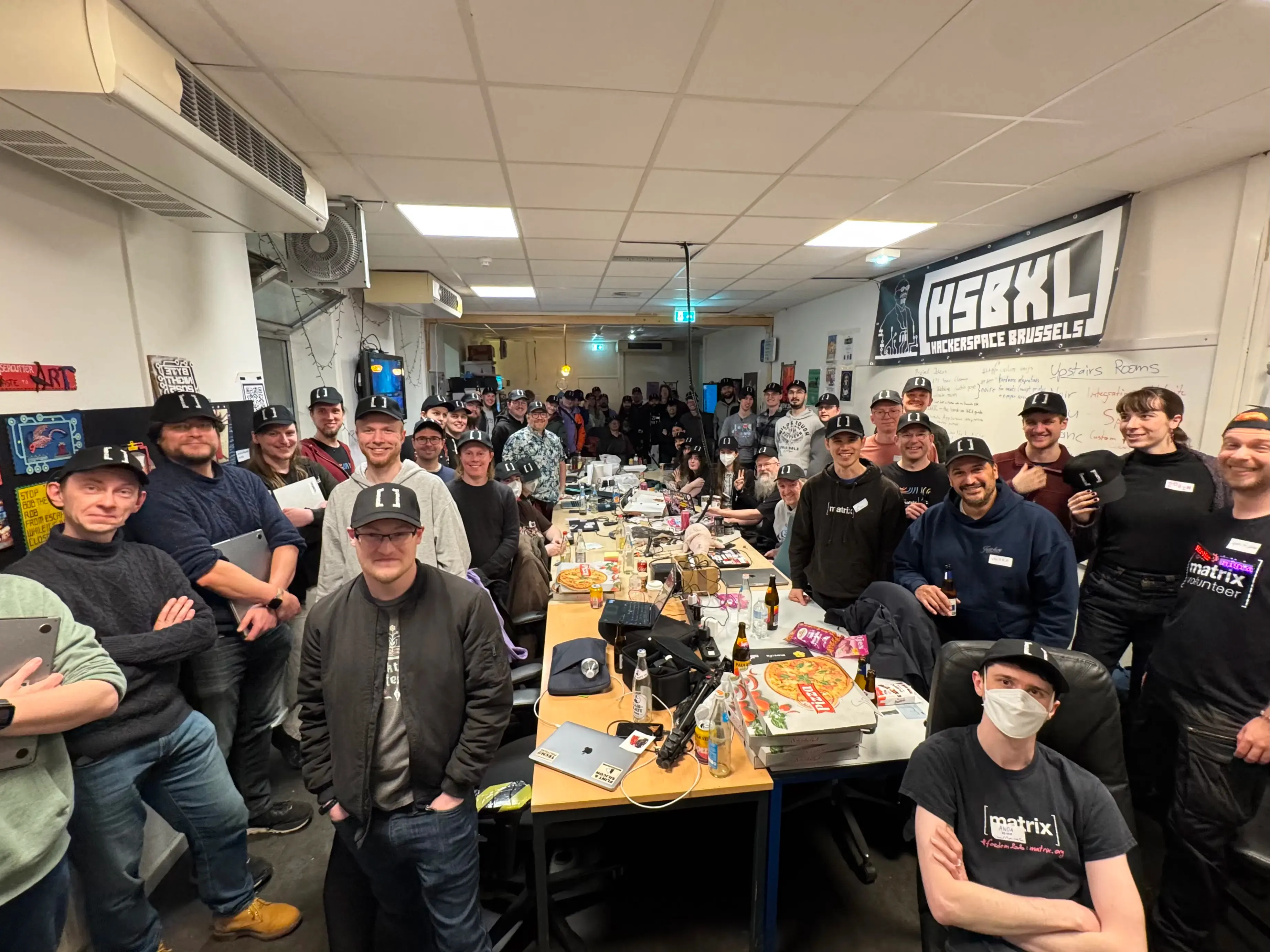 A picture of about a thousand people in a room, looking at the camera and smiling. All of them are wearing Matrix hats.